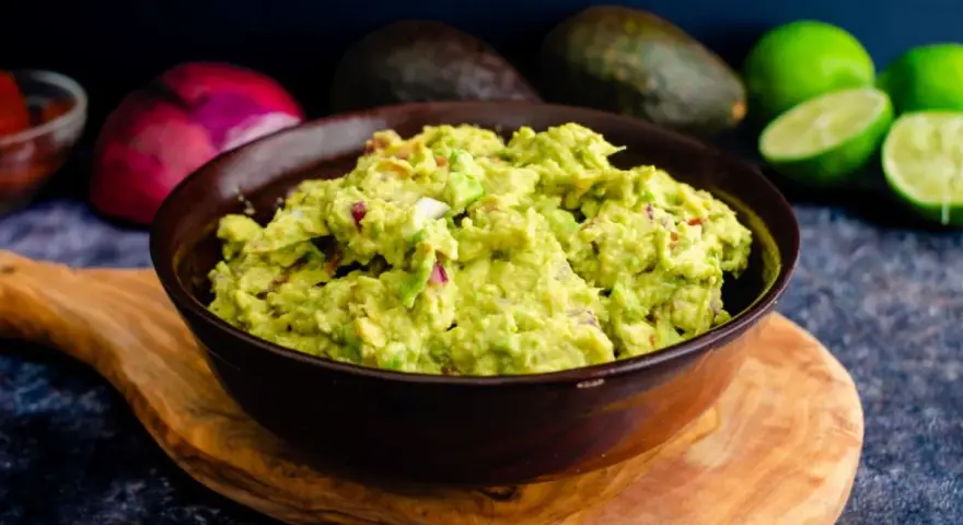 Miseczka guacamole z awokado, cebulą i limonką na drewnianej desce.