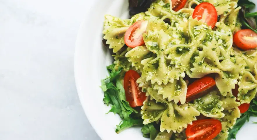 Pyszna sałatka z makaronem farfalle w sosie pesto, z pomidorkami koktajlowymi i świeżą sałatą.