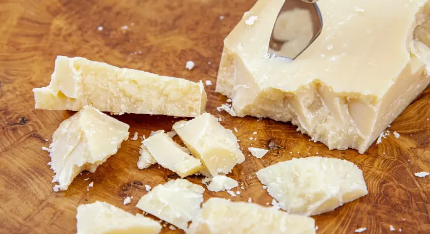 Kawałki sera Grana Padano na drewnianej desce. Czy Grana Padano to parmezan? Ten twardy ser dojrzewa długo, podobnie jak parmezan.