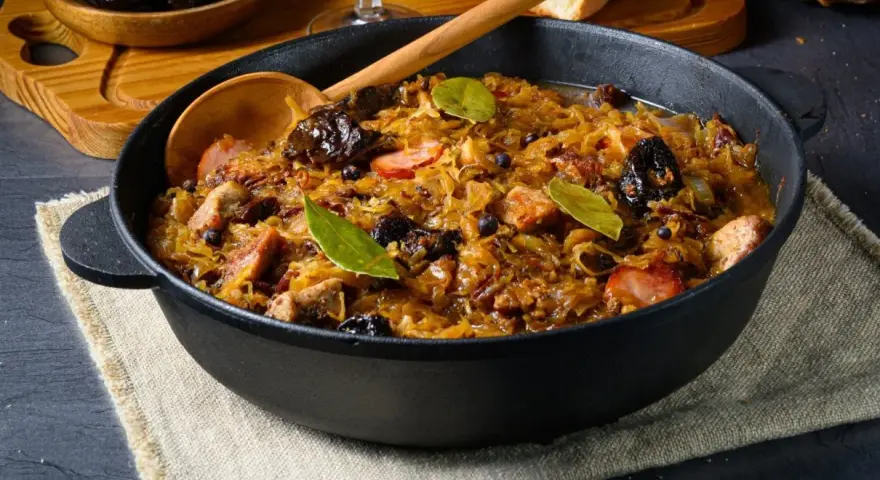 Pyszny bigos w żeliwnym naczyniu, z widocznymi kawałkami mięsa, śliwkami i liśćmi laurowymi. Idealne danie, gdy zastanawiasz się, jakie mięso do bigosu wybrać.