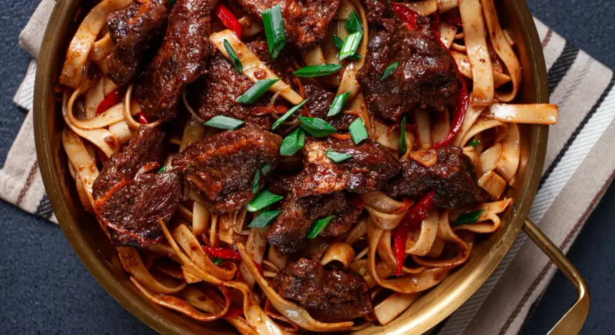 Pyszne wolowina po seczuańsku z makaronem, papryczkami chili i szczypiorkiem w złotej misie.