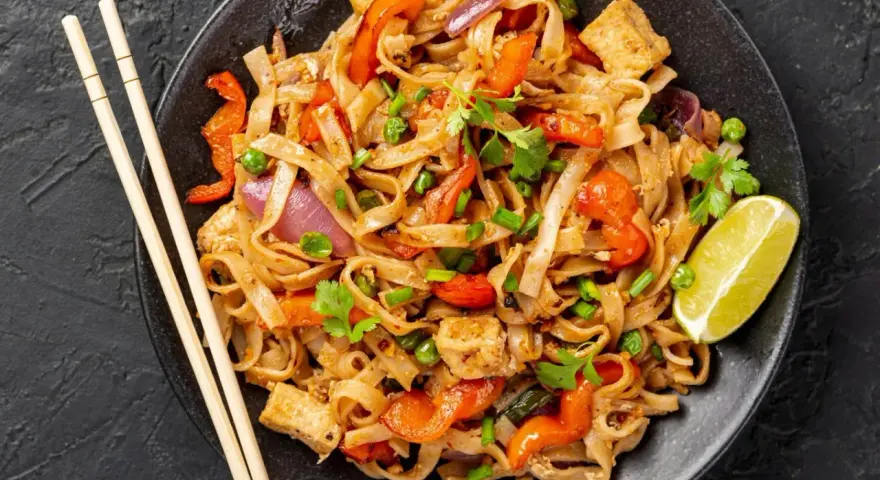 Pyszny pad thai z kurczakiem, warzywami i makaronem ryżowym, udekorowany kolendrą i ćwiartką limonki.