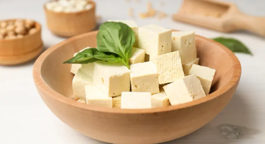 Kostki tofu w drewnianej misce z bazylią. Czy tofu można jeść na surowo? Tak, to świetna baza do sałatek i przekąsek.