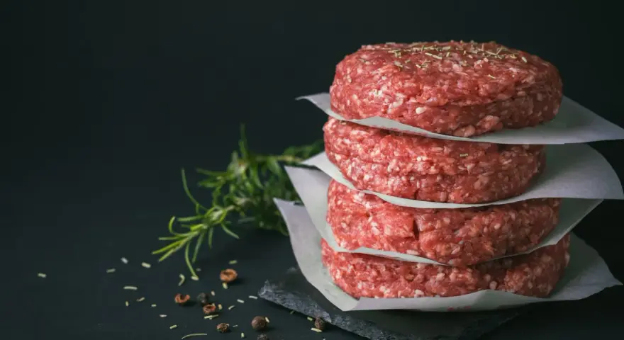 Stos świeżego, mielonego mięsa na burgery, przyprawionego ziołami i pieprzem, gotowe do grillowania.