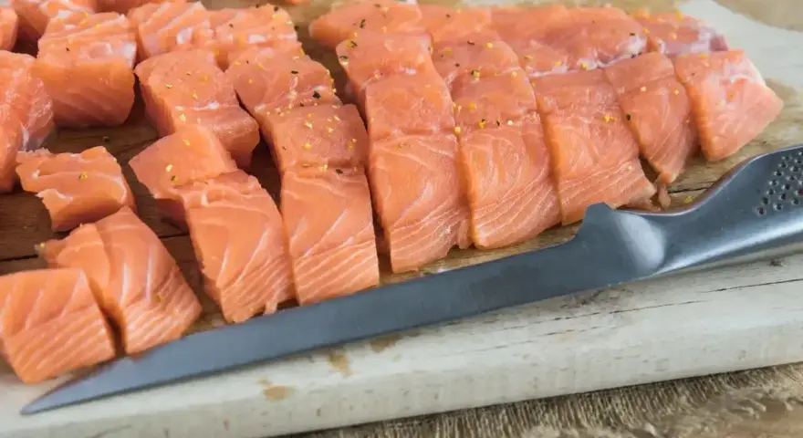 Świeży, pokrojony łosoś do sushi, doprawiony, leży na desce obok noża. Idealny łosoś do sushi.