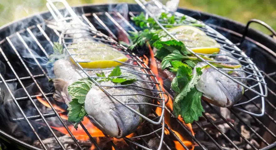 Dwie ryby na grillu, z cytryną i ziołami, unoszą się nad ogniem. Idealna jaka ryba na grilla na letni wieczór.