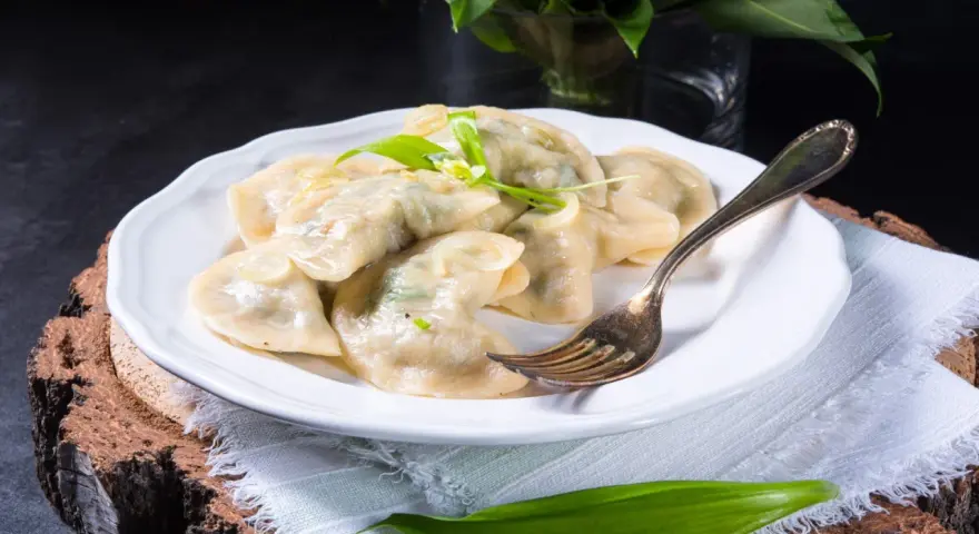 Pyszne pierogi ze szpinakiem i serem, udekorowane czosnkiem niedźwiedzim, na białym talerzu.