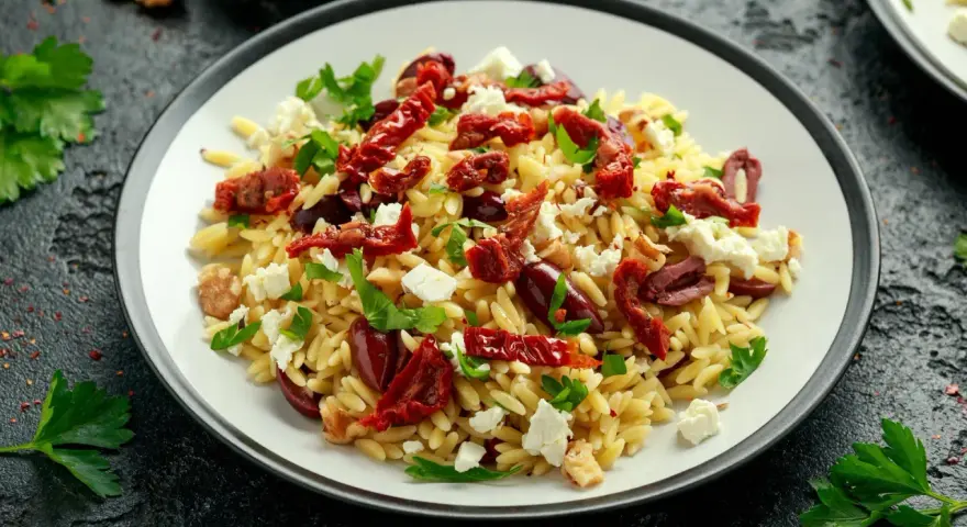 Pyszna sałatka z makaronem orzo, z suszonymi pomidorami, oliwkami, fetą i natką pietruszki.