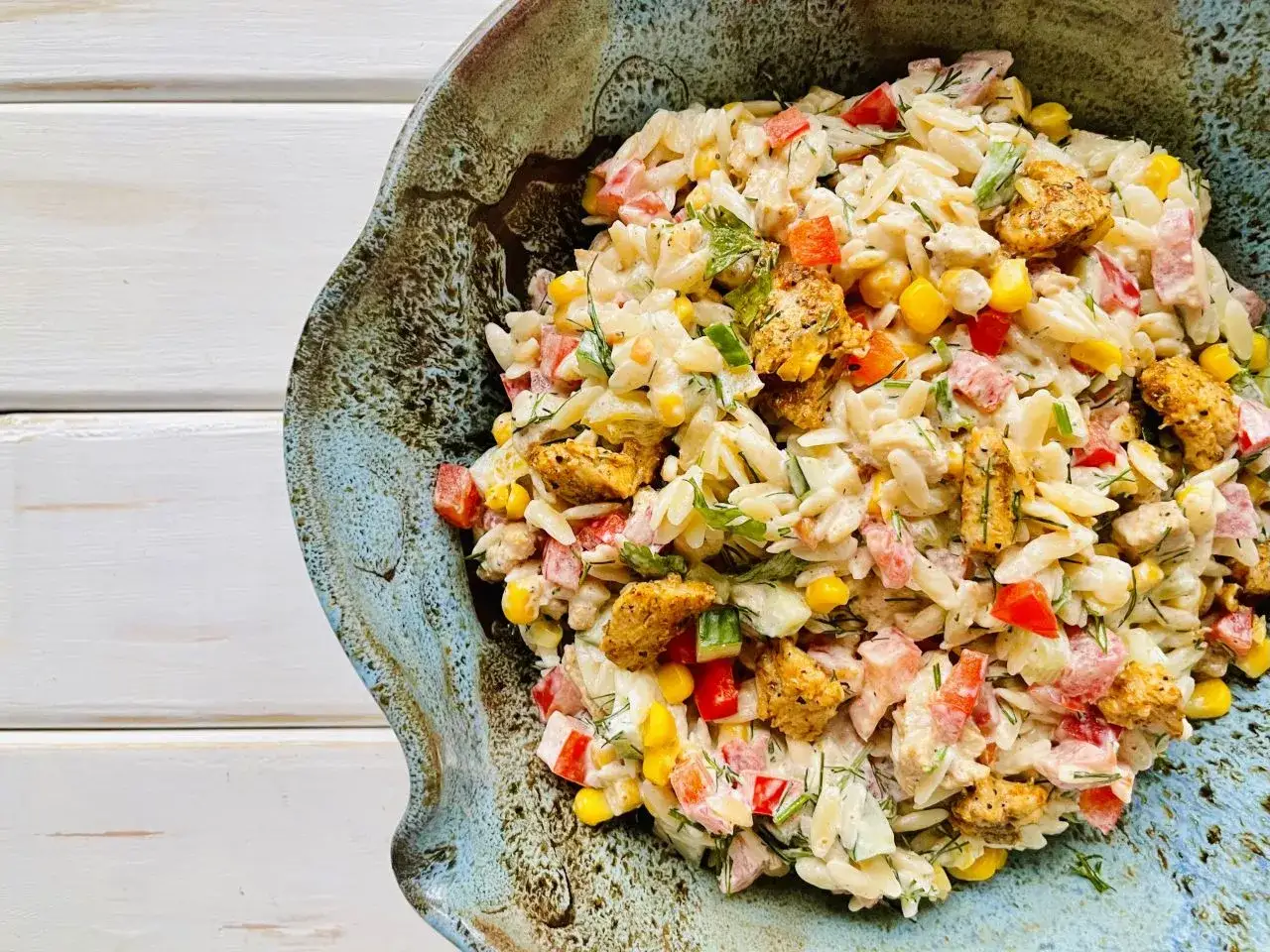 Pyszna sałatka z makaronem orzo, kurczakiem, kukurydzą i papryką, podana w ozdobnej misie.