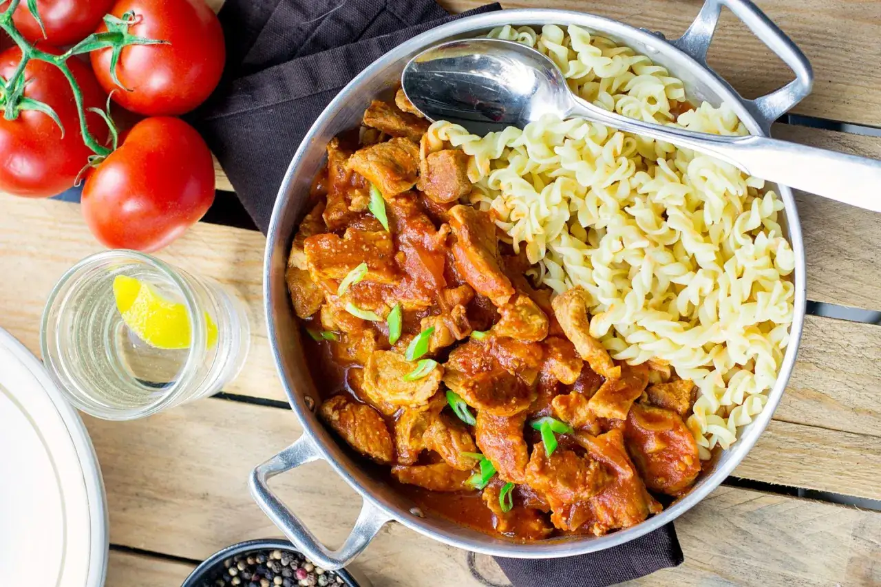 Mięciutki schab a'la strogonow w sosie pomidorowym z makaronem fusilli. Obok pomidory, szklanka wody z cytryną i przyprawy.