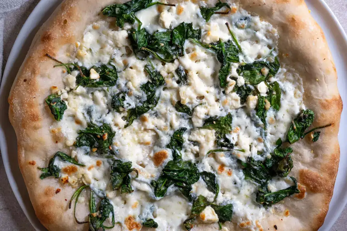 Pyszna pizza ze szpinakiem i białym serem, z chrupiącym, złotym brzegiem.