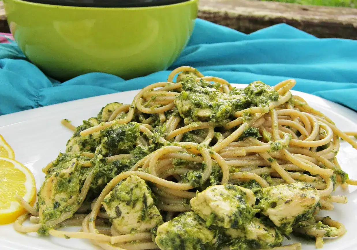 Pyszny makaron z pesto i kurczakiem, podany z plasterkami cytryny.