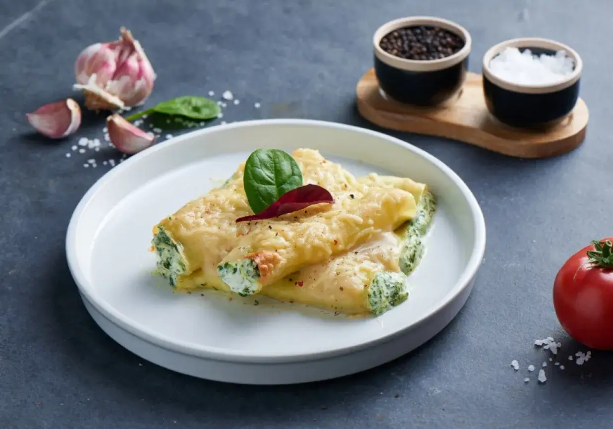 Pyszne cannelloni ze szpinakiem, zapieczone pod serem, z dodatkiem czosnku i pomidora.