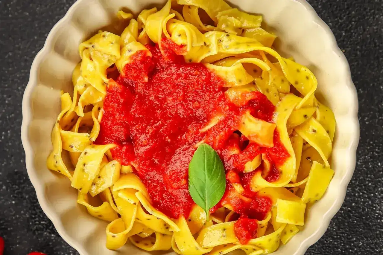 Pyszne dania z makaronem: szerokie tagliatelle z sosem pomidorowym i listkiem bazylii.
