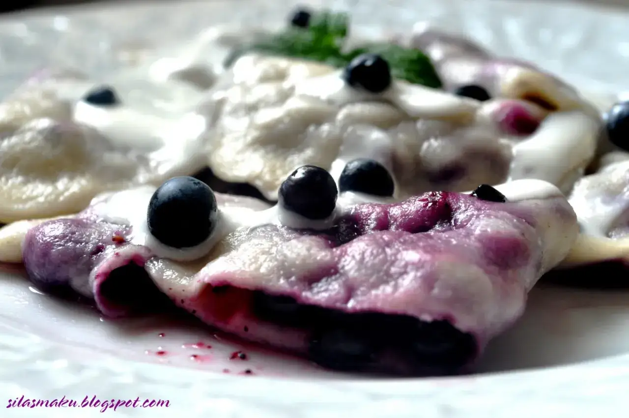 Pyszne pierogi z jagodami, polane śmietaną i ozdobione świeżymi owocami. Letnia uczta na talerzu.