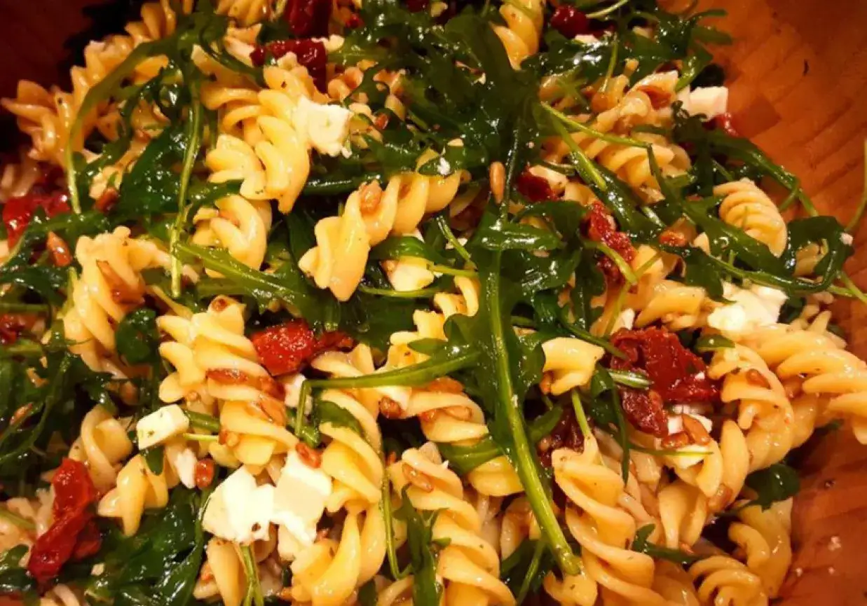 Pyszna sałatka z makaronem fusilli, rukolą, kawałkami sera feta i słodkimi, suszonymi pomidorami.