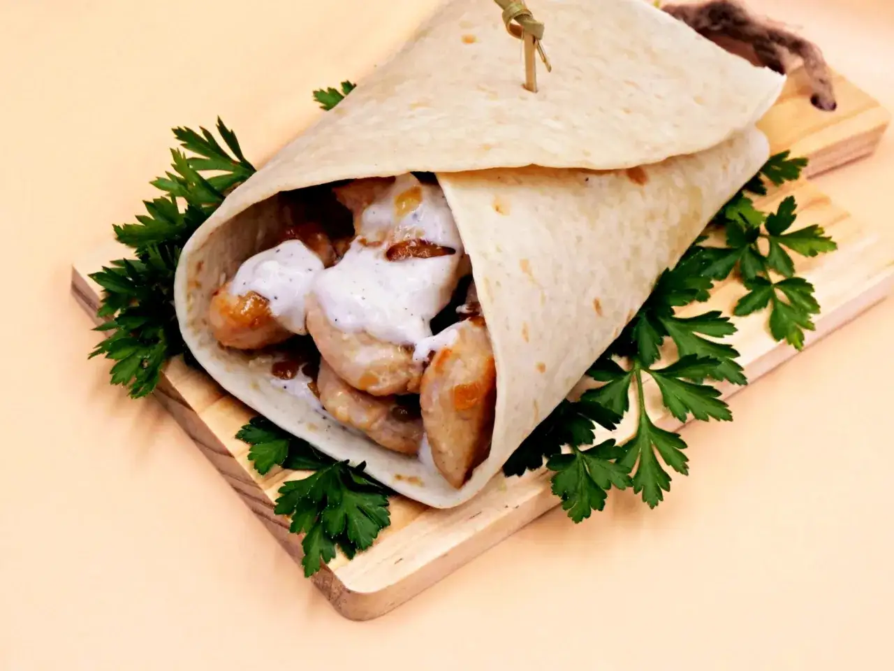 Pyszna tortilla z kurczakiem, polana kremowym sosem, ozdobiona natką pietruszki, podana na drewnianej desce.