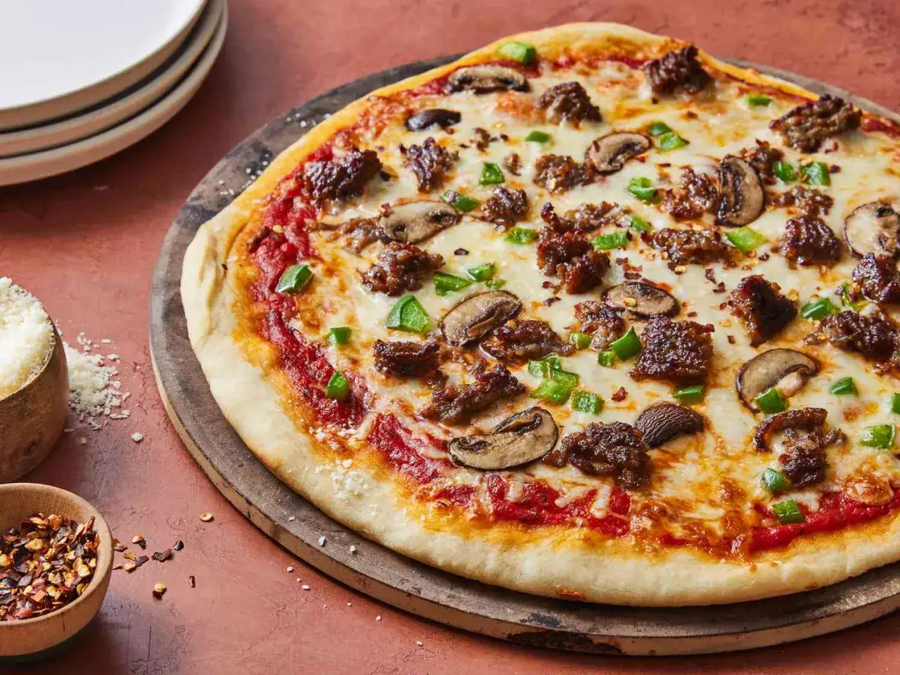 Pyszna pizza na cienkim cieście z mielonym mięsem, pieczarkami i zieloną papryką.