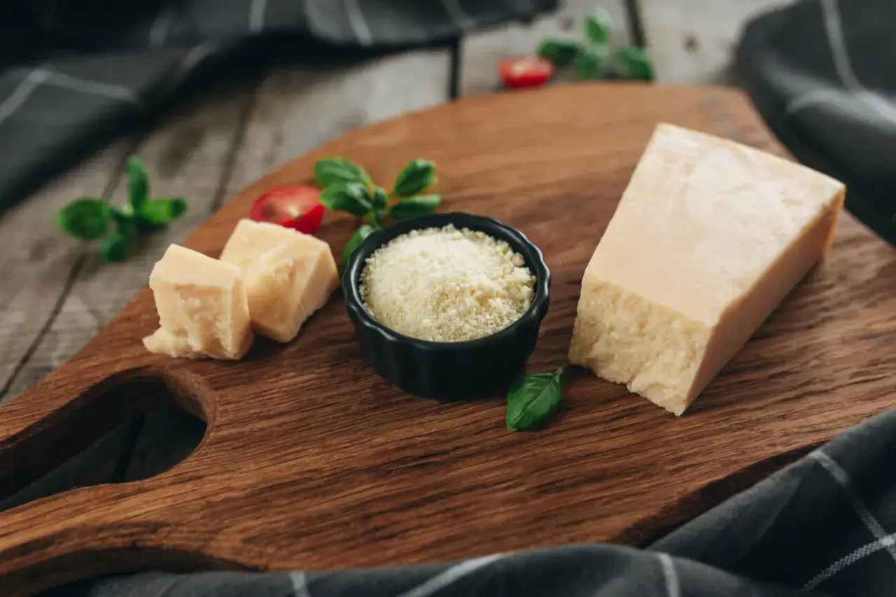 Kawałki parmezanu i starty ser w miseczce, idealne jako jaki ser do carbonary. Dodatki: bazylia i pomidorki.